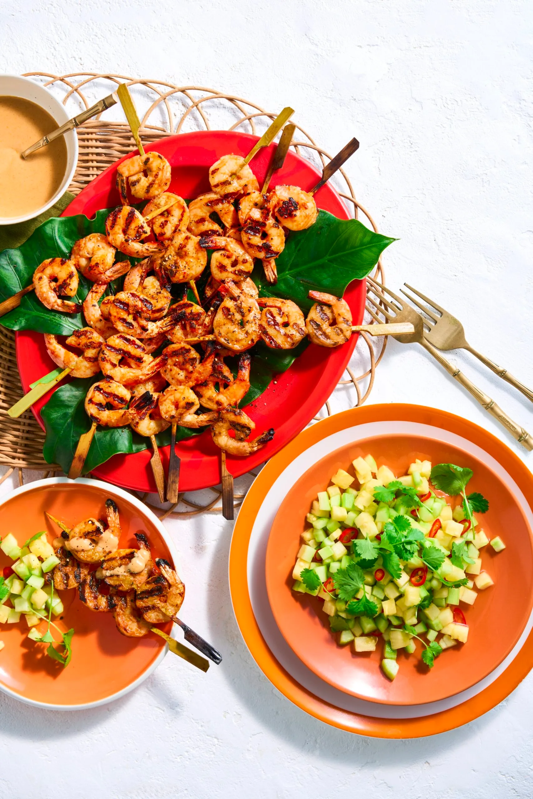 assiette rouge de crevettes sur des brochettes avec une feuille de bananier en dessous. assiette d'orange avec salade d'ananas et de concombre hachée sur le côté