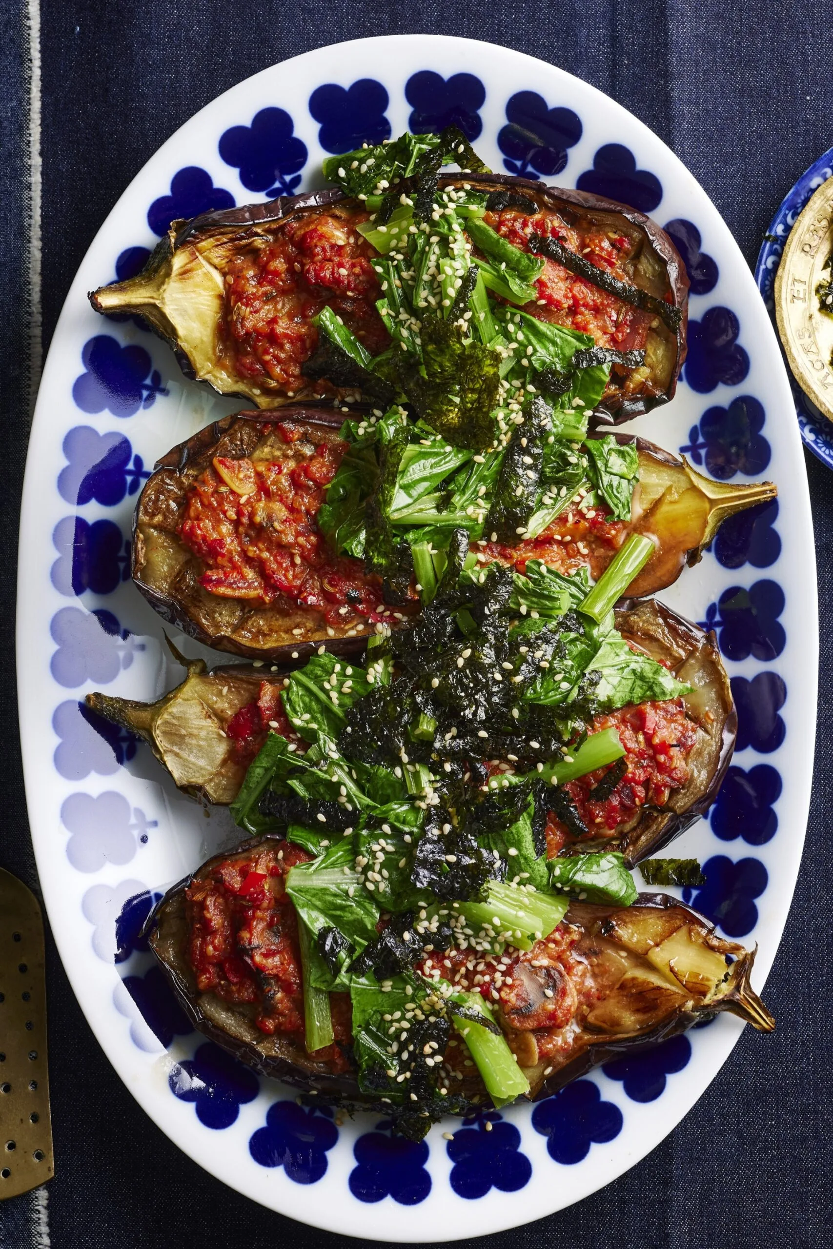 photo de quatre tranches d'aubergines cuites avec de la sauce miso et des légumes verts asiatiques dessus. Une assiette bleue avec des fleurs sur le pourtour