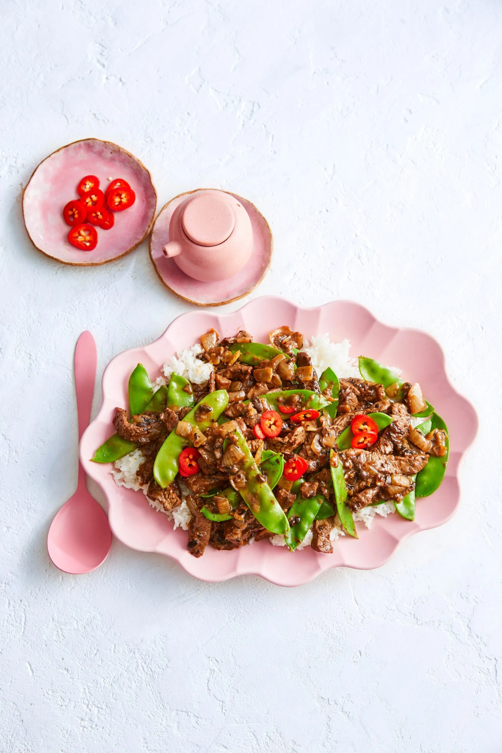 Sauté de bœuf et de haricots noirs avec pois mange-tout et piment sur le dessus dans un bol rose festonné