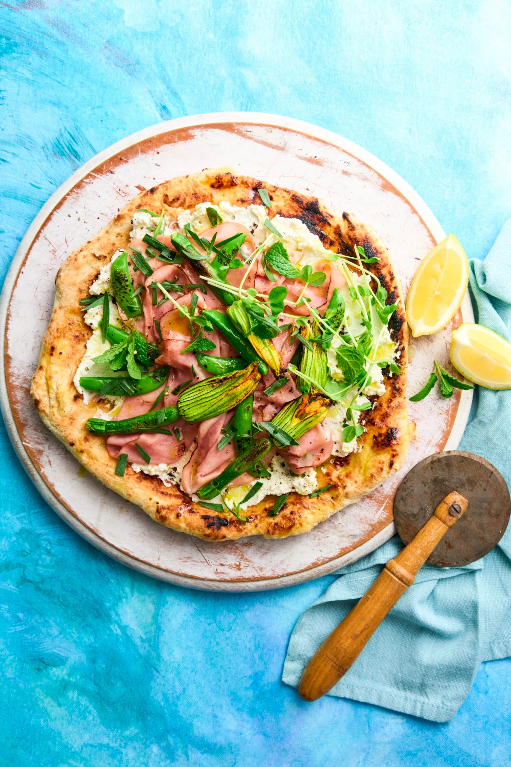 pizza printanière avec fleurs de courgettes, fromage de chèvre et jambon dessus. coupe-pizza rustique et citron sur le côté