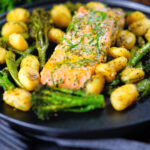 Plateau de filet de saumon cuit au four avec pesto, légumes verts et gnocchis servis sur une assiette noire.