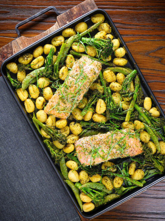 Plateau de filet de saumon cuit au four avec pesto, légumes verts et gnocchis servis sur une plaque à pâtisserie.