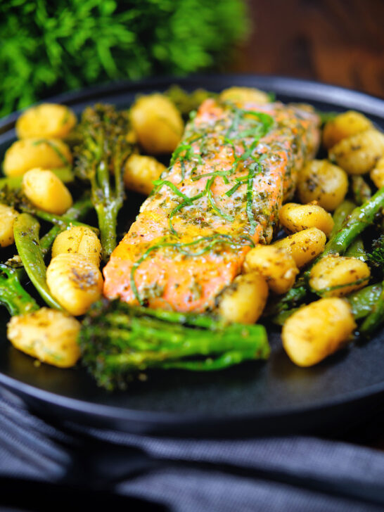 Plateau de filet de saumon cuit au four avec pesto, légumes verts et gnocchis servis sur une assiette noire.