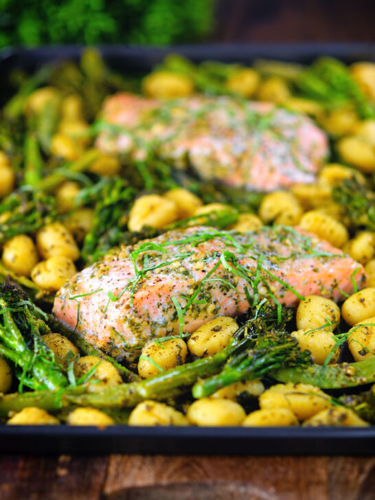 Plateau de filet de saumon cuit au four avec pesto, légumes verts et gnocchis servis sur une plaque à pâtisserie.