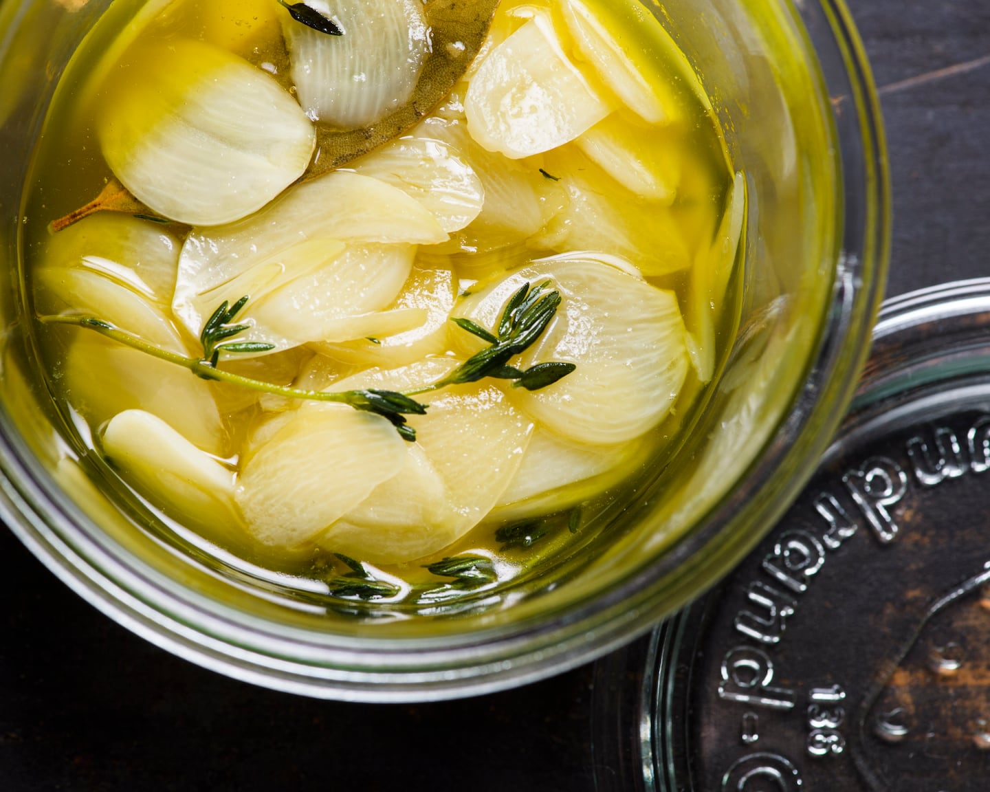 Un petit récipient en verre avec des tranches d'ail et des herbes dans l'huile d'olive.