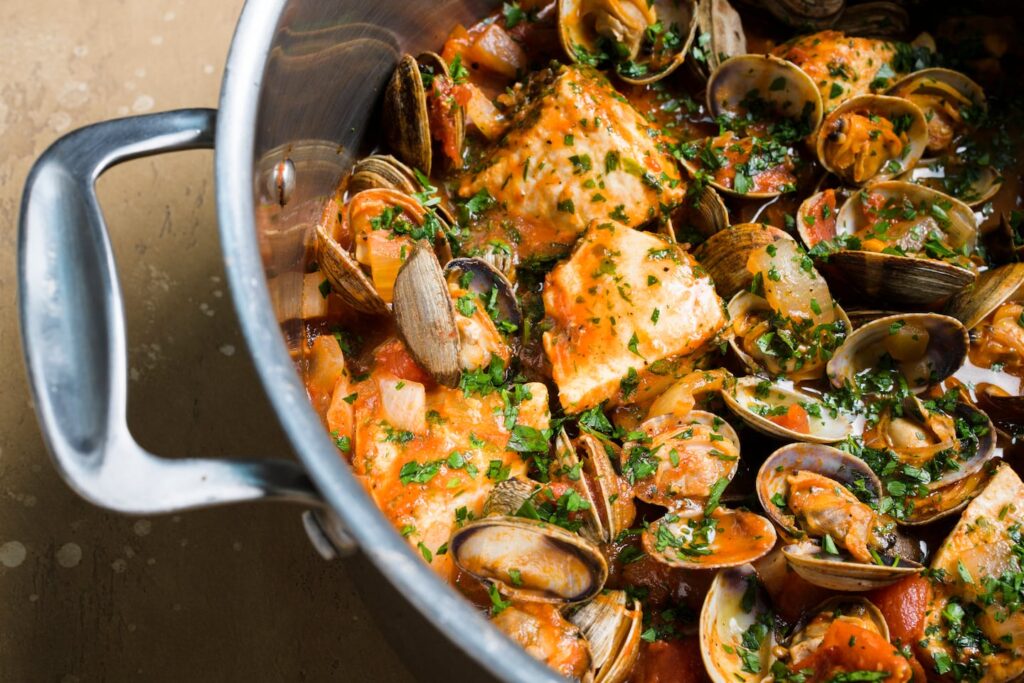 A silver pan with shell fish in a tomato sauce. It's garnished with herbs.