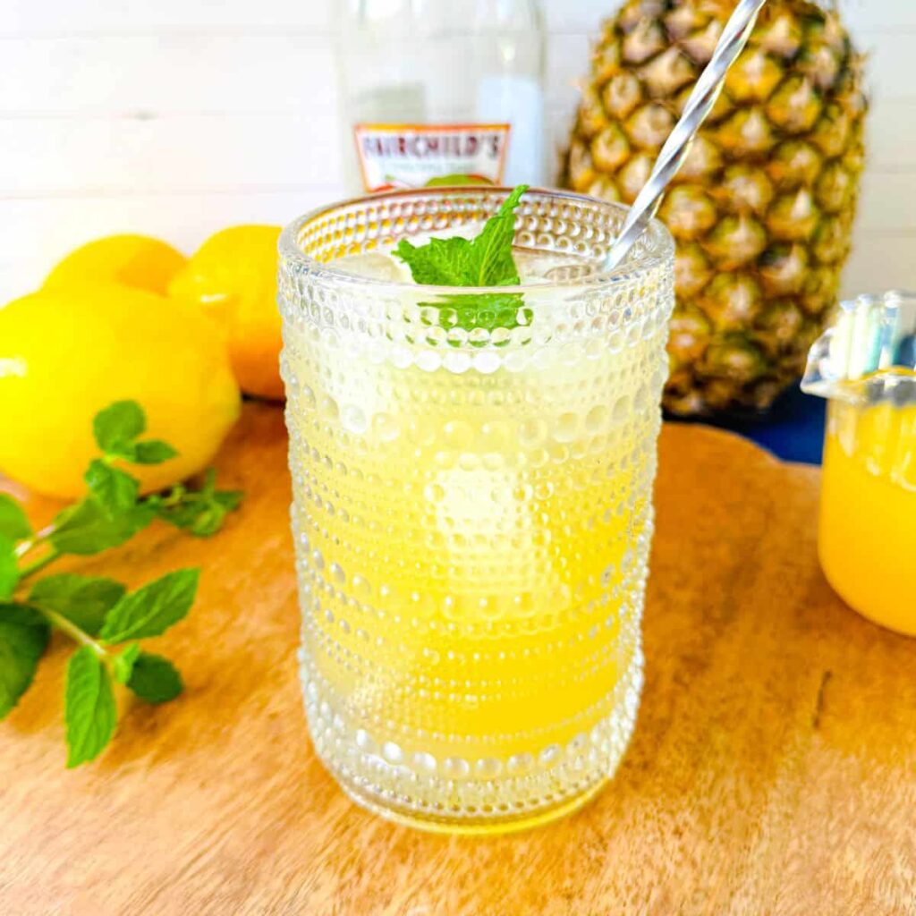 apple cider vinegar drink with pineapple and mint garnish in a dotted glass cup