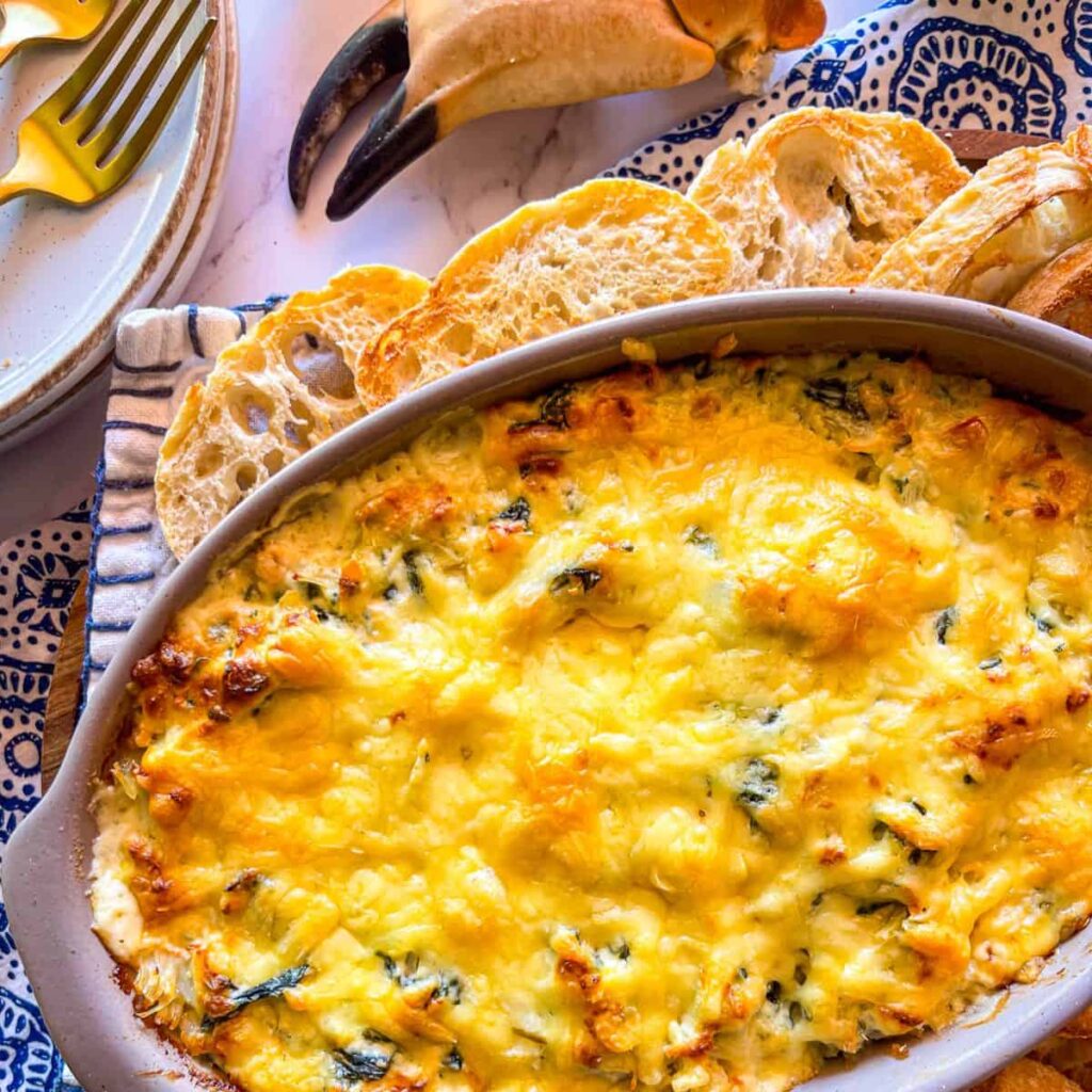 Finished Seafood Dip topped with melted cheese and served in a bowl with baguette slices.