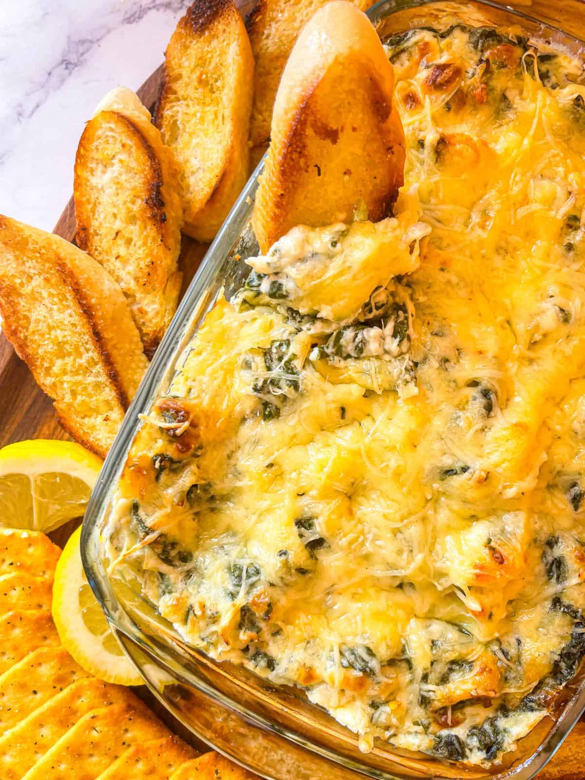 plat de cuisson en verre rempli de trempette aux épinards recouverte de fromage fondu avec des baguettes grillées sur le côté.