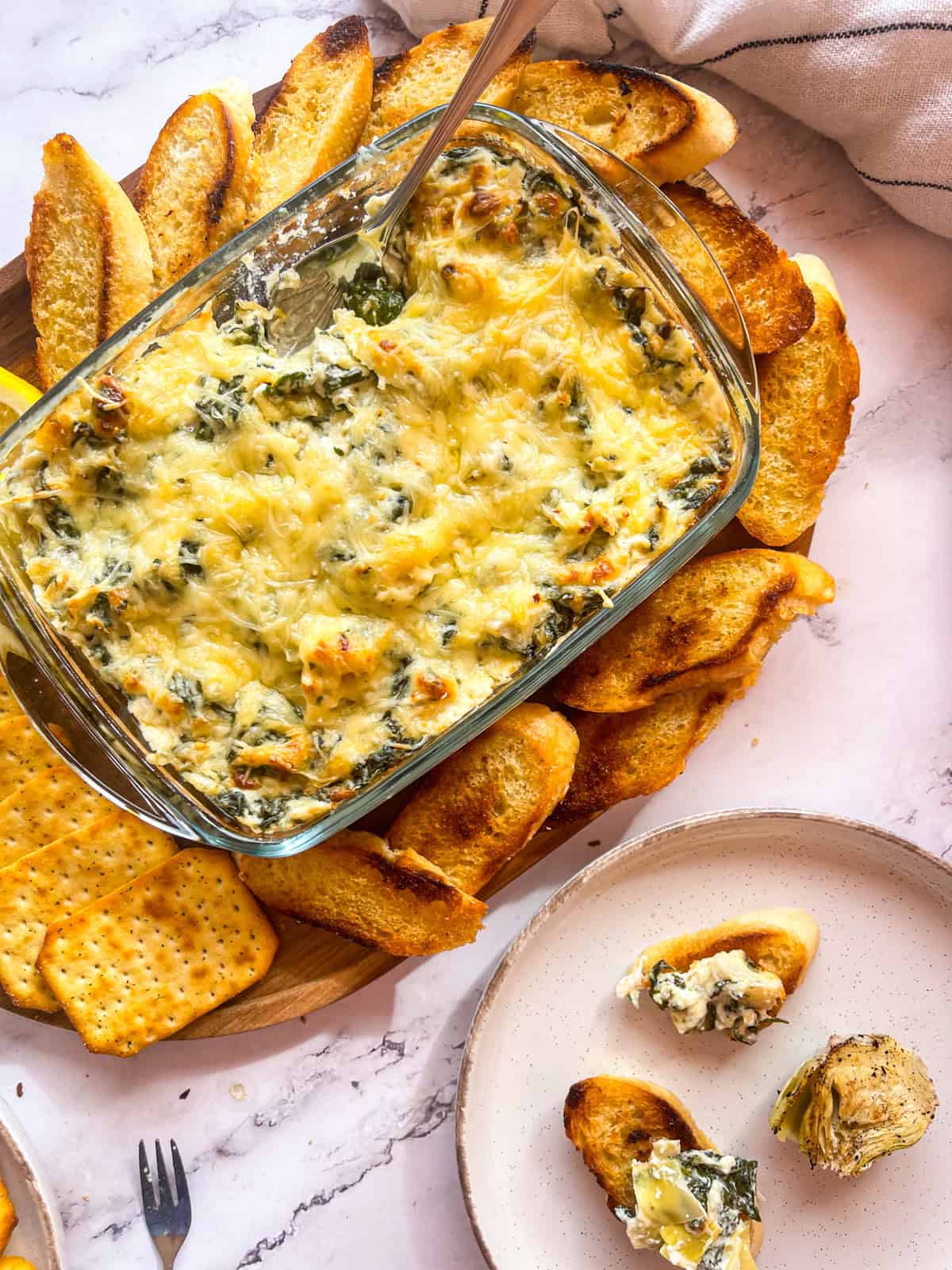 Trempette aux épinards servie sur un plateau avec des baguettes grillées et des craquelins.