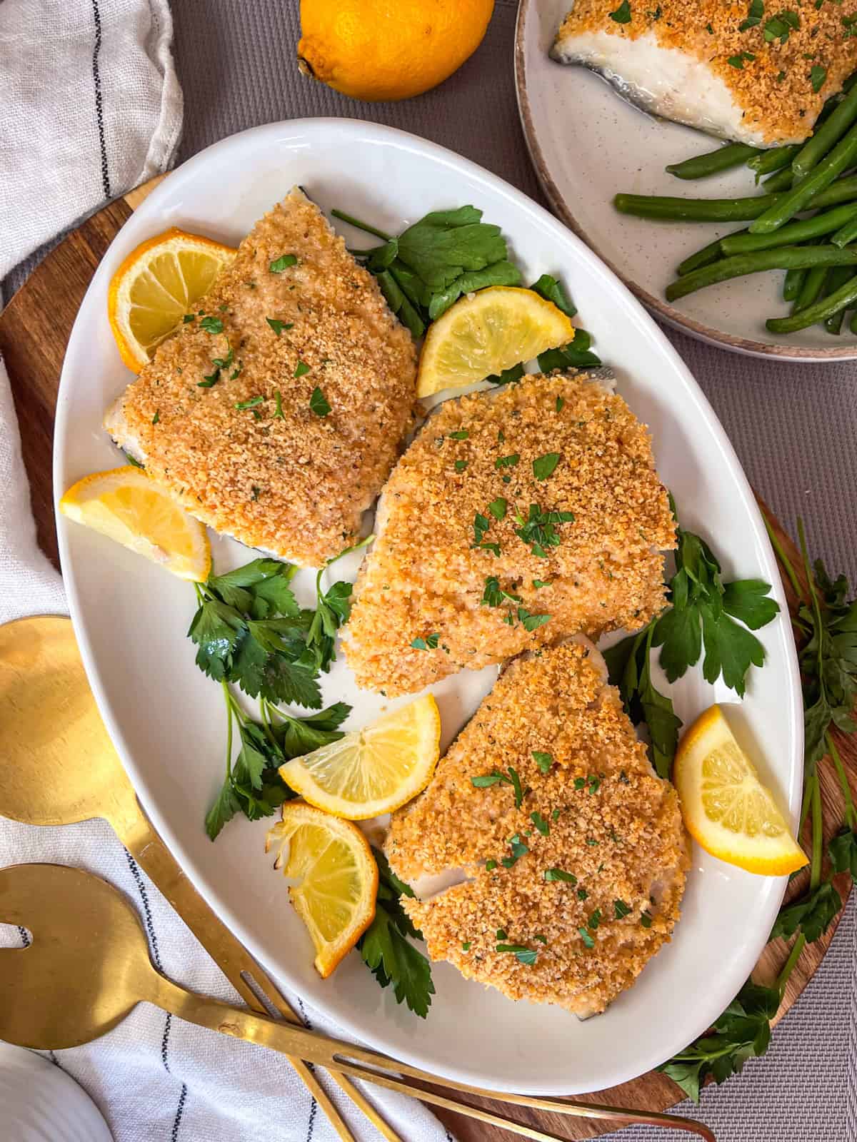 poisson cuit au four avec de la chapelure sur un plateau blanc garni de persil et de citrons.