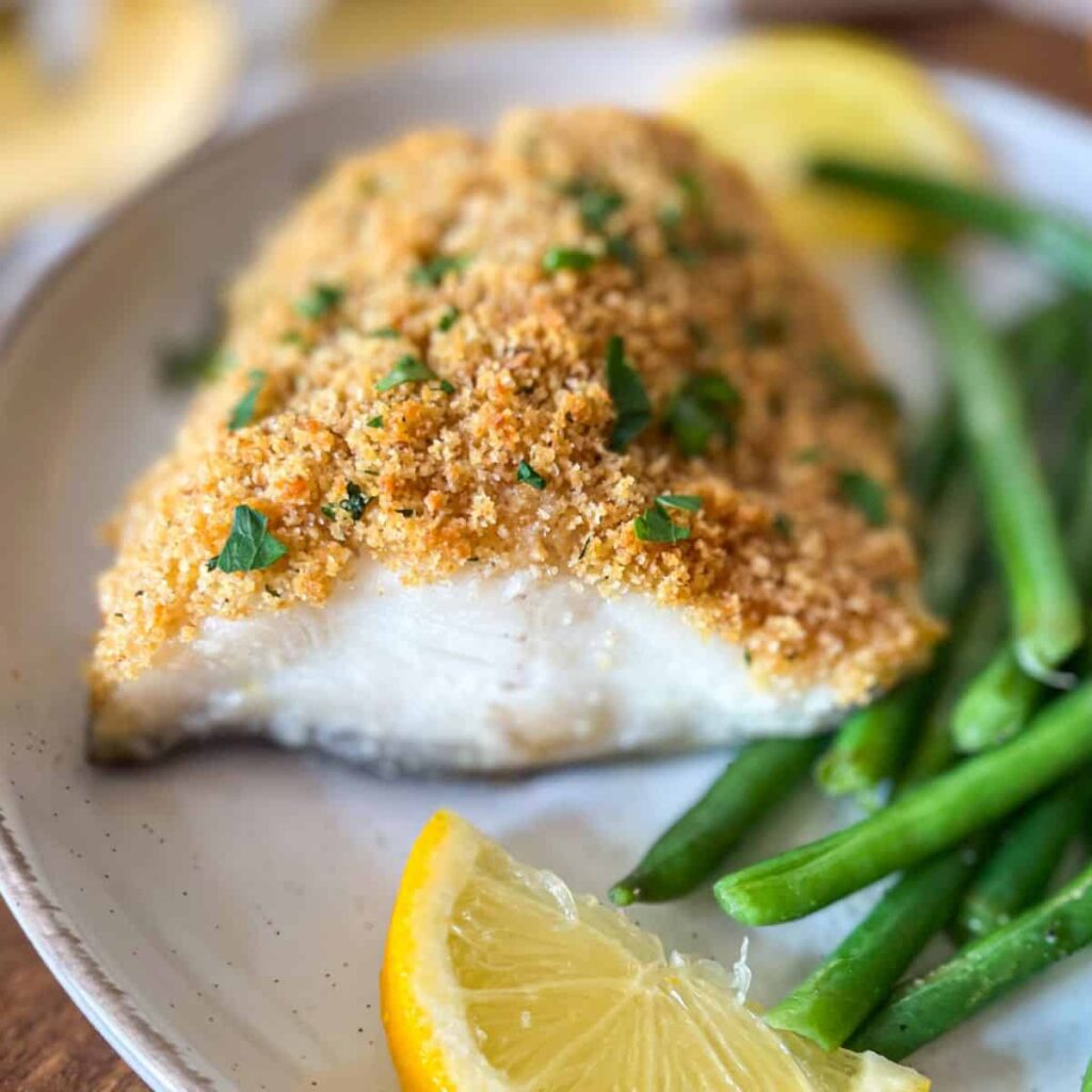 baked black cod on a white platter garnished with parsley and lemons.