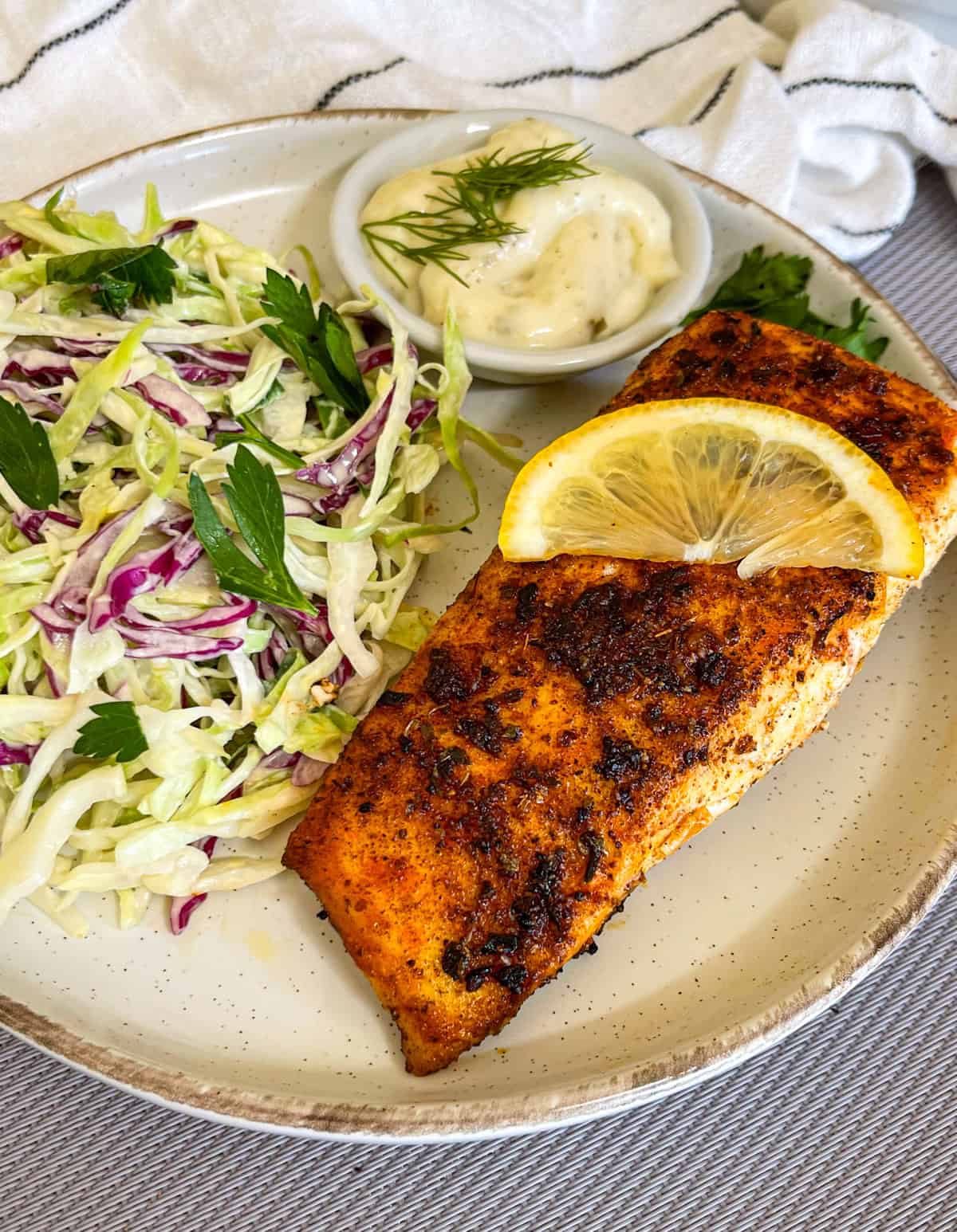 Poisson noirci servi sur une assiette avec salade de chou, sauce tartare et quartiers de citron.