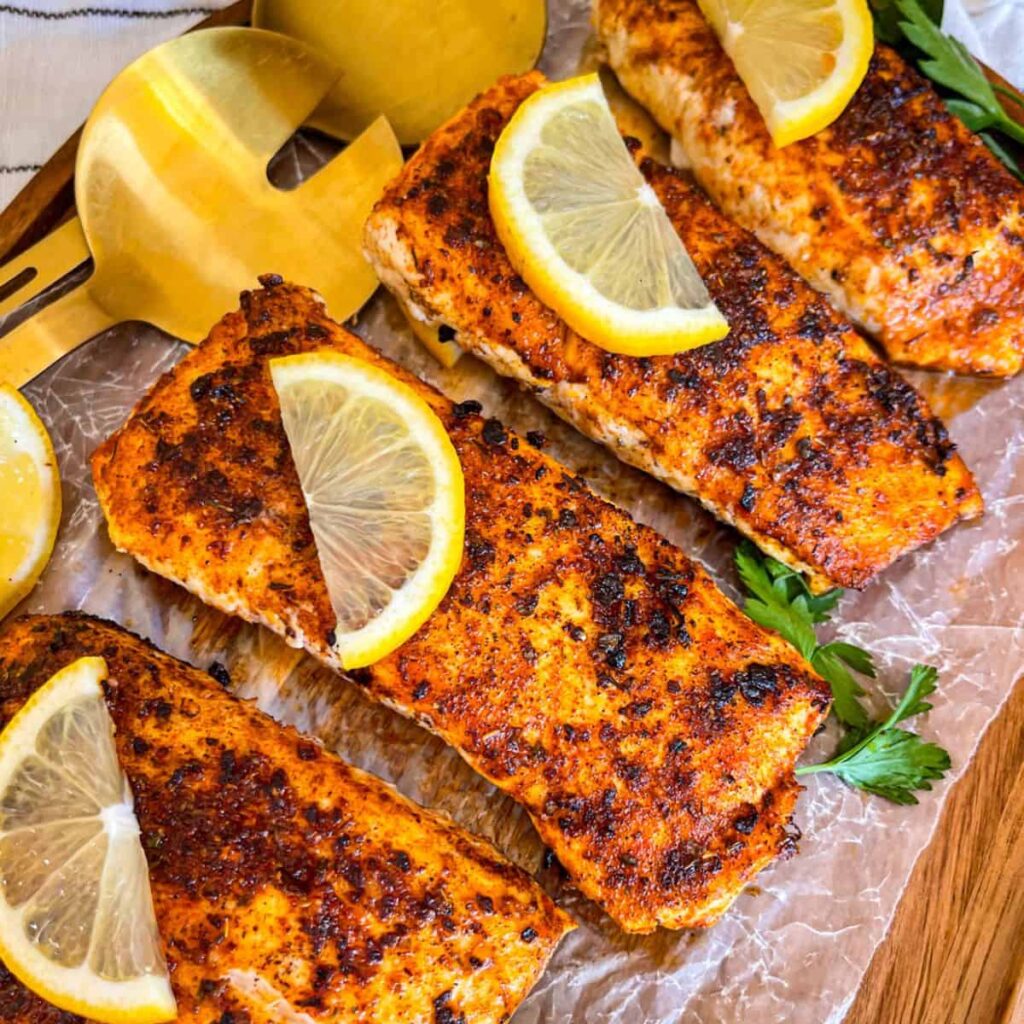 4 Blackened halibut fillets served on a platter with lemon wedges and parsley.