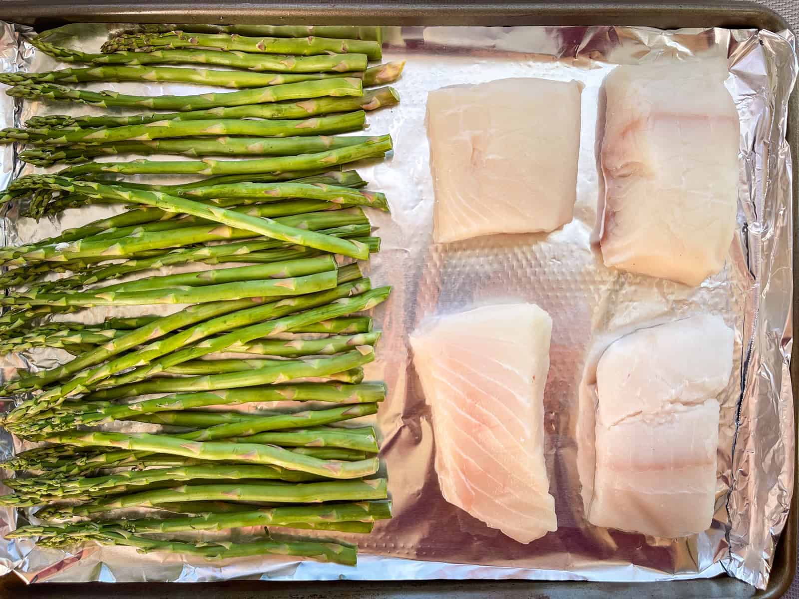 4 morceaux de flétan disposés sur une plaque à pâtisserie avec des asperges disposées sur la moitié de la plaque.