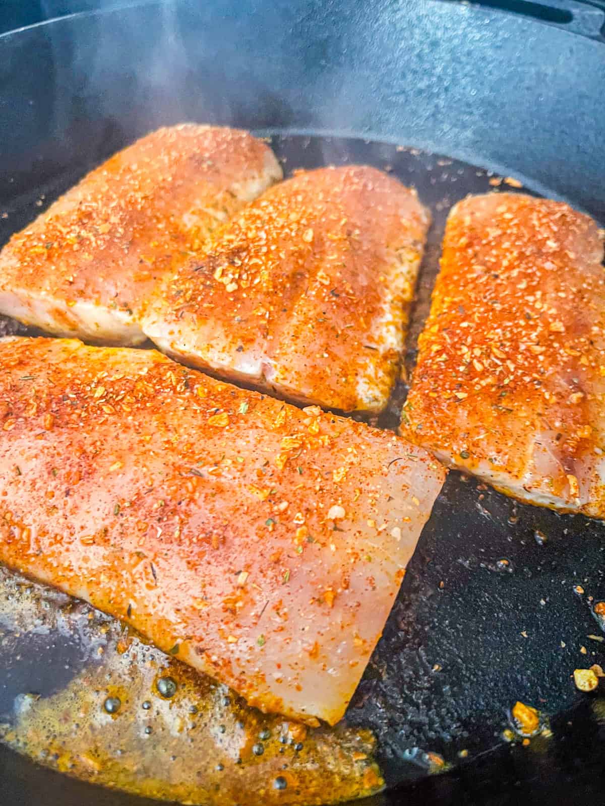 Filets de poisson assaisonnés grésillant dans une poêle en fonte.