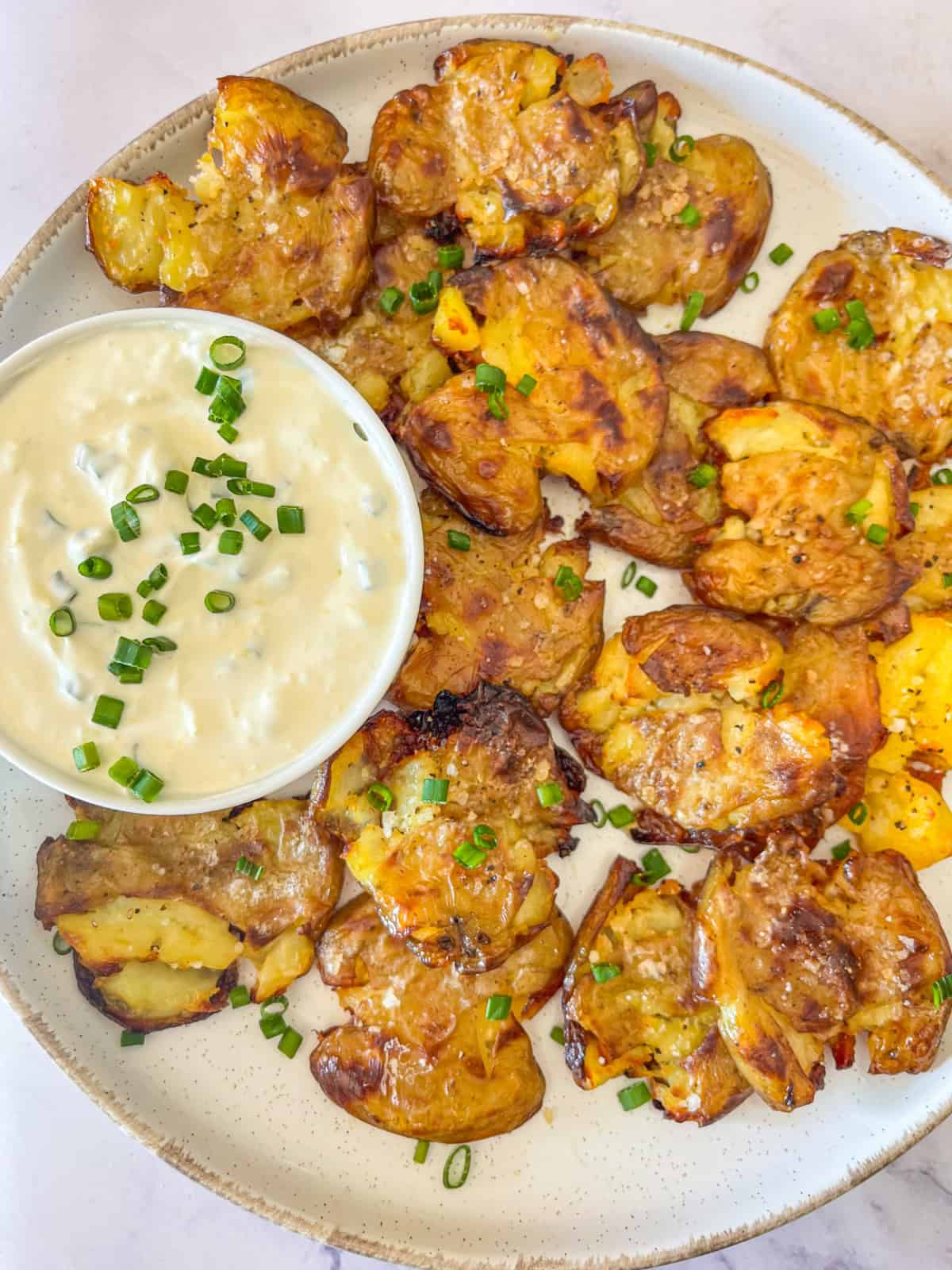 Pommes de terre écrasées croustillantes garnies de sauce à la crème sure et de ciboulette.