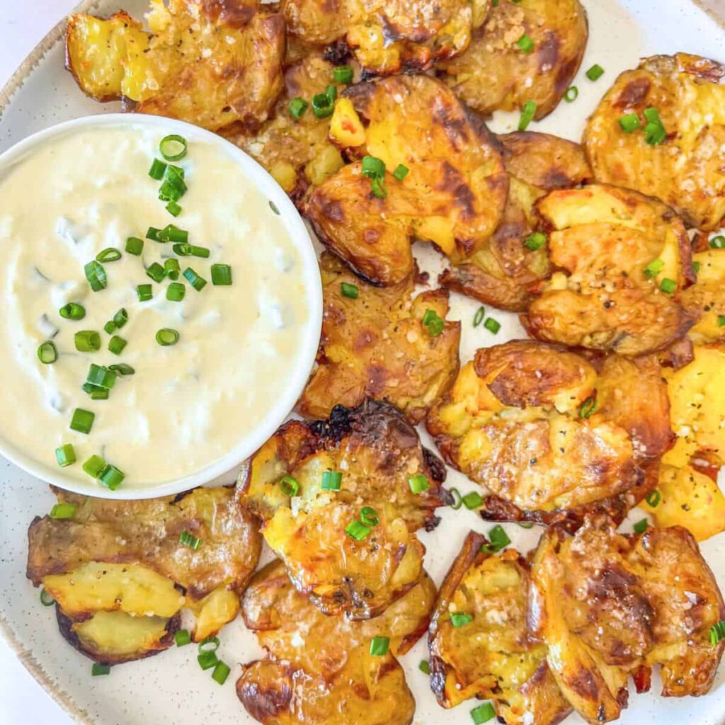 crispy smashed potato on a platter with sour cream and chive dip.