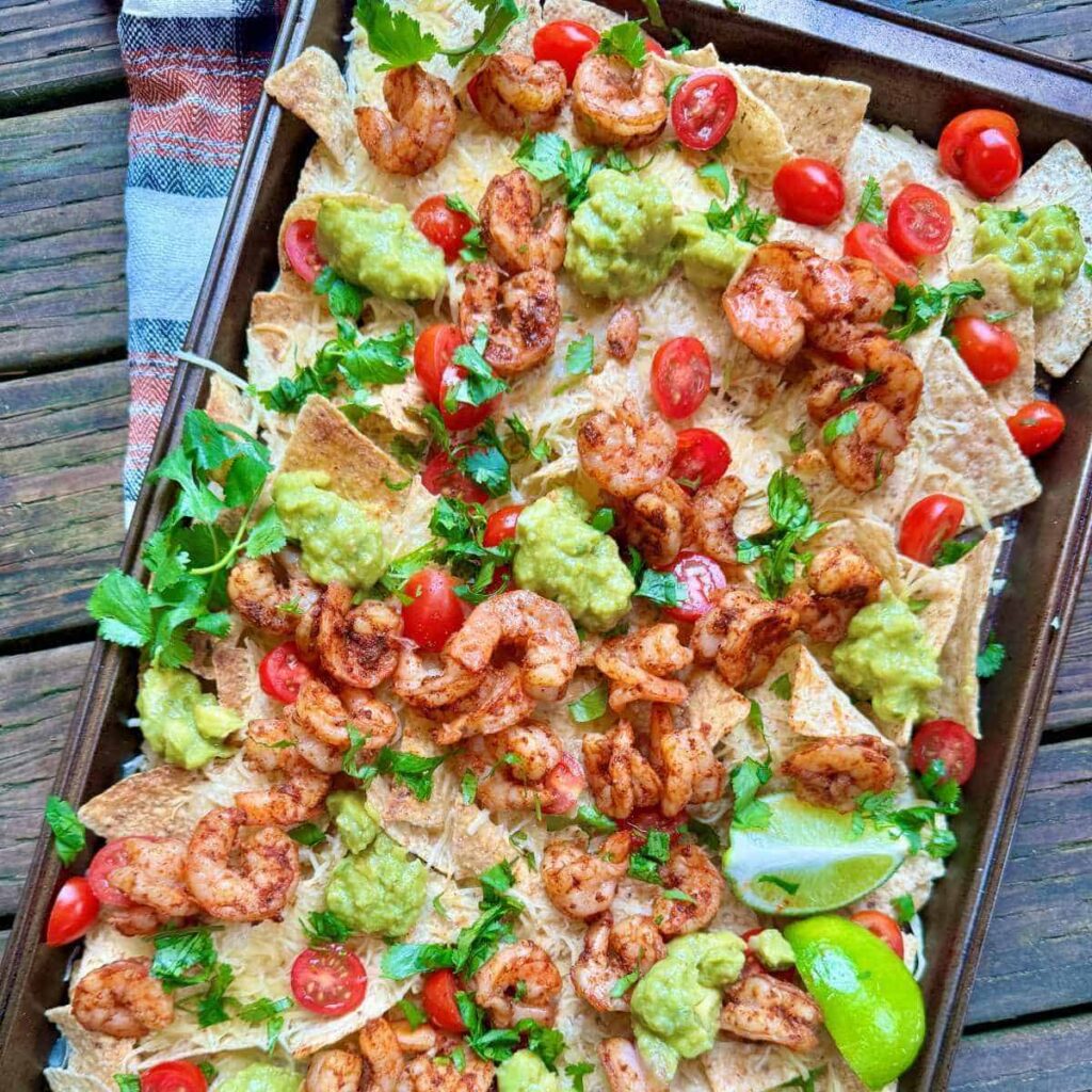 blackened shrimp nachos on a sheet pan with cilantro lime guacamole and cherry tomatoes