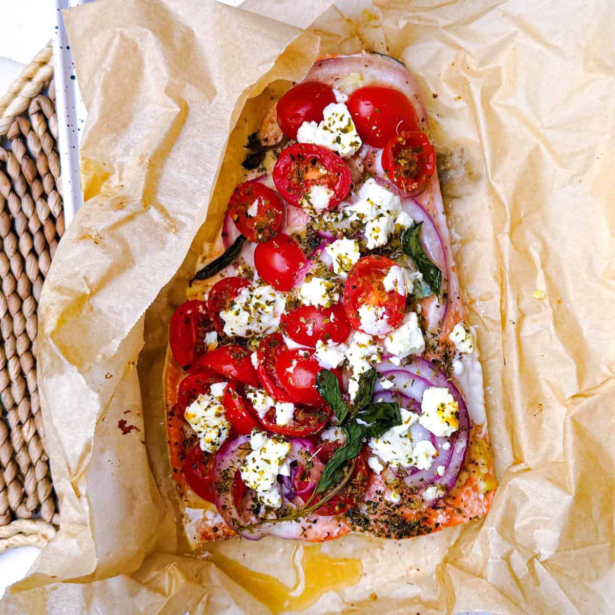 poisson en papillote enveloppé dans du papier sulfurisé avec feta, tomates, oignon rouge et herbes