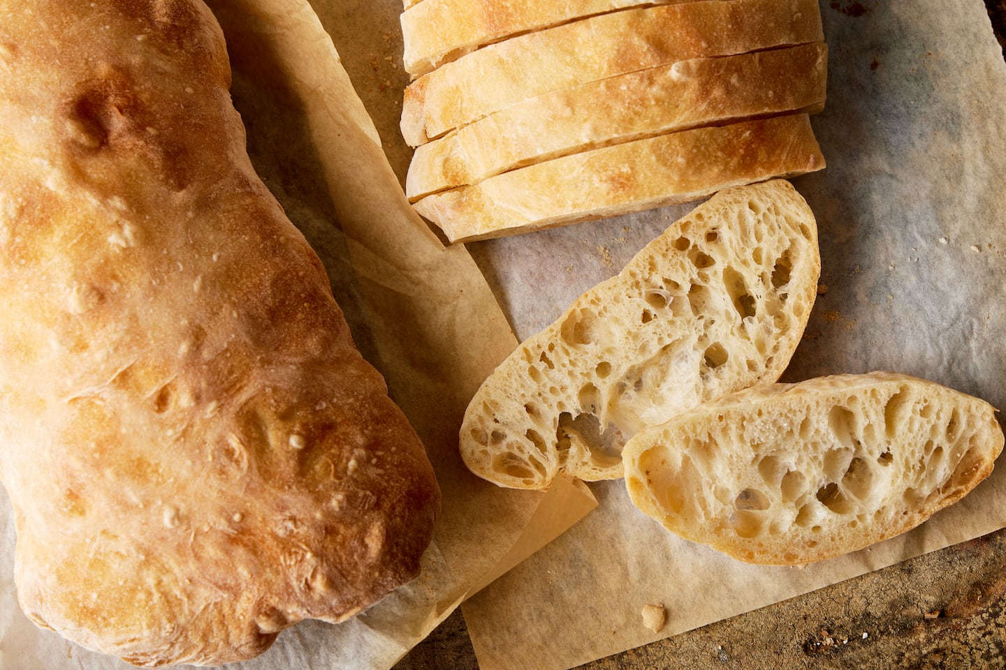 Deux miches de pain ciabatta disposées sur du papier parchemin doré. Le pain de gauche n’est pas coupé et le pain de droite a été tranché.