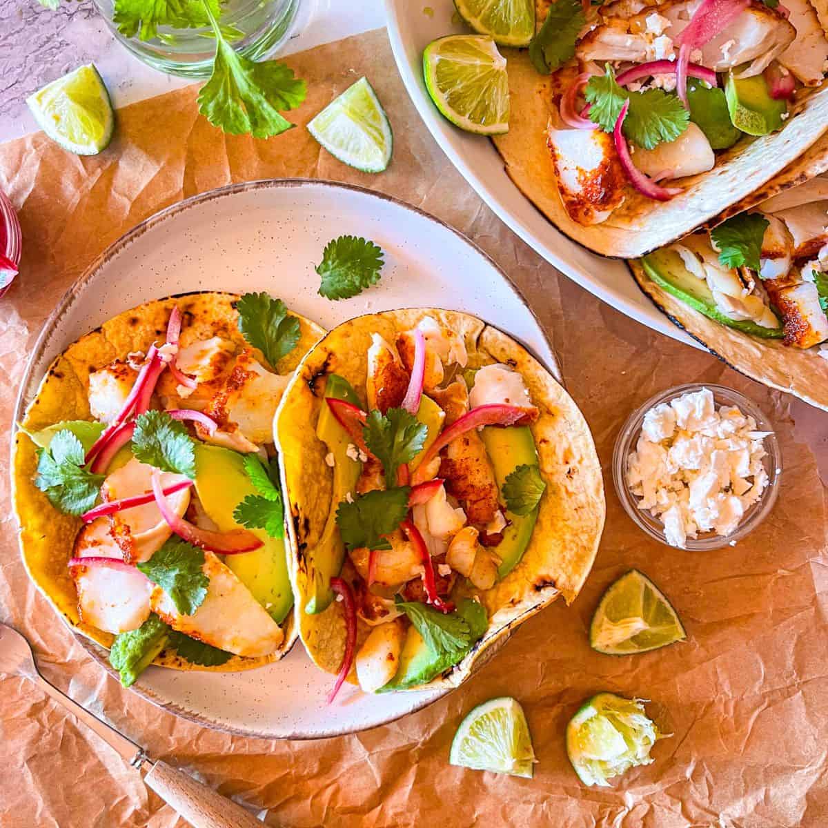 2 plates of fish tacos with limes and cheese around it.
