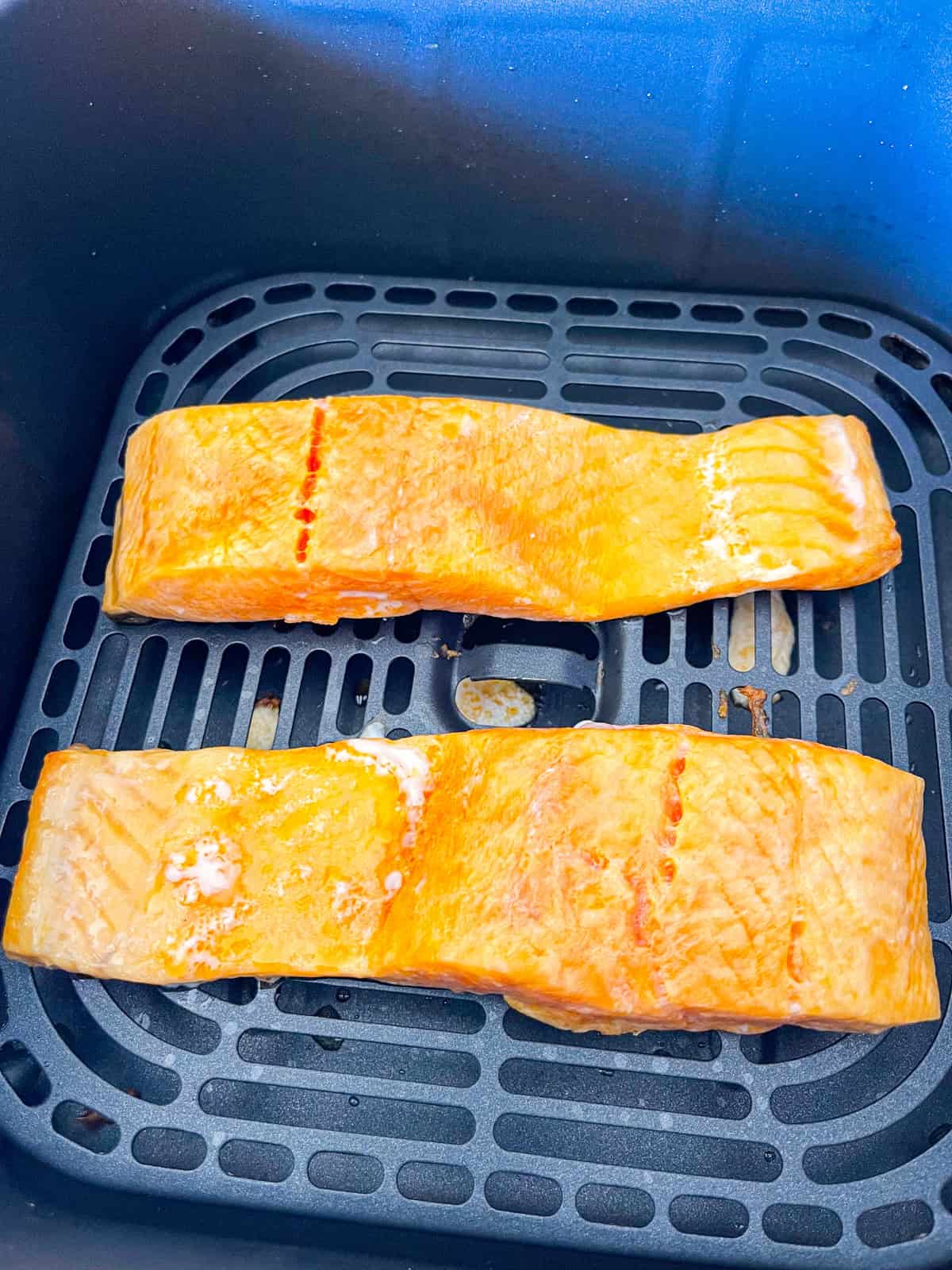 2 morceaux de saumon cuisant dans le panier de la friteuse à air.