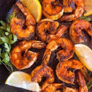 Blackened shrimp cooked in a skillet and garnished with lemon and parsley.
