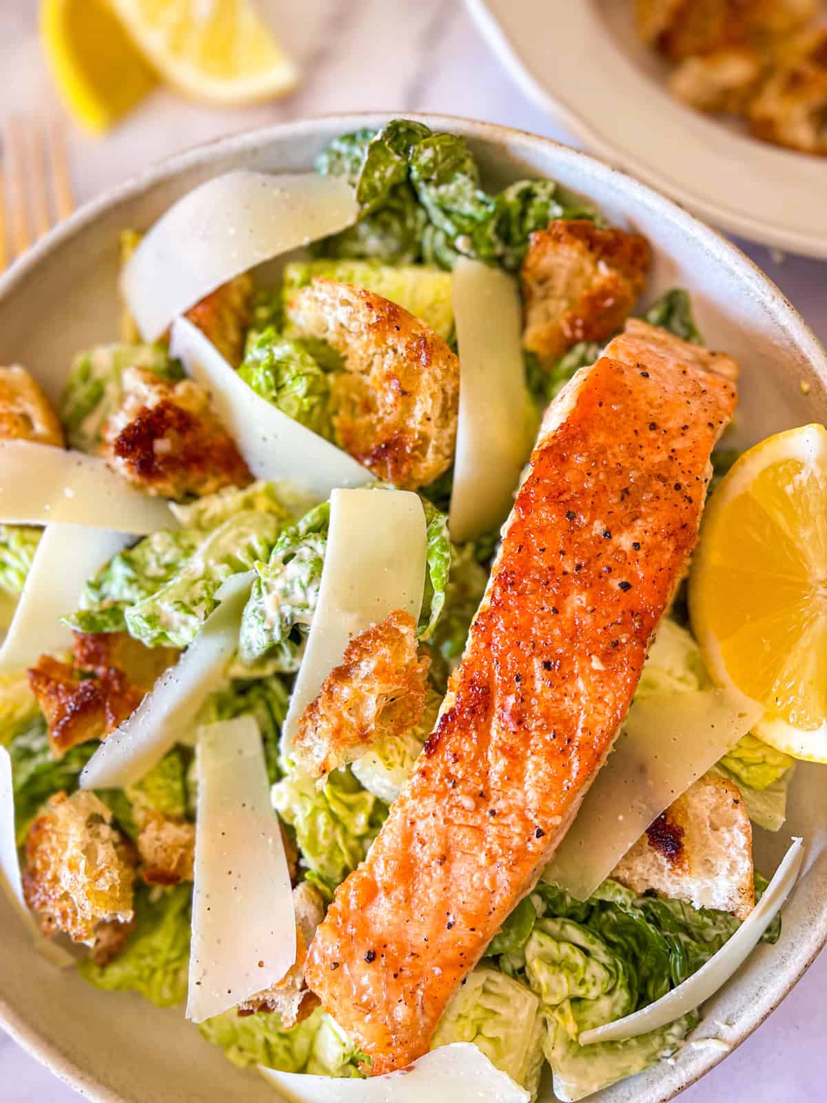 Filet de saumon sur une salade César sur une assiette avec croûtons et parmesan râpé.
