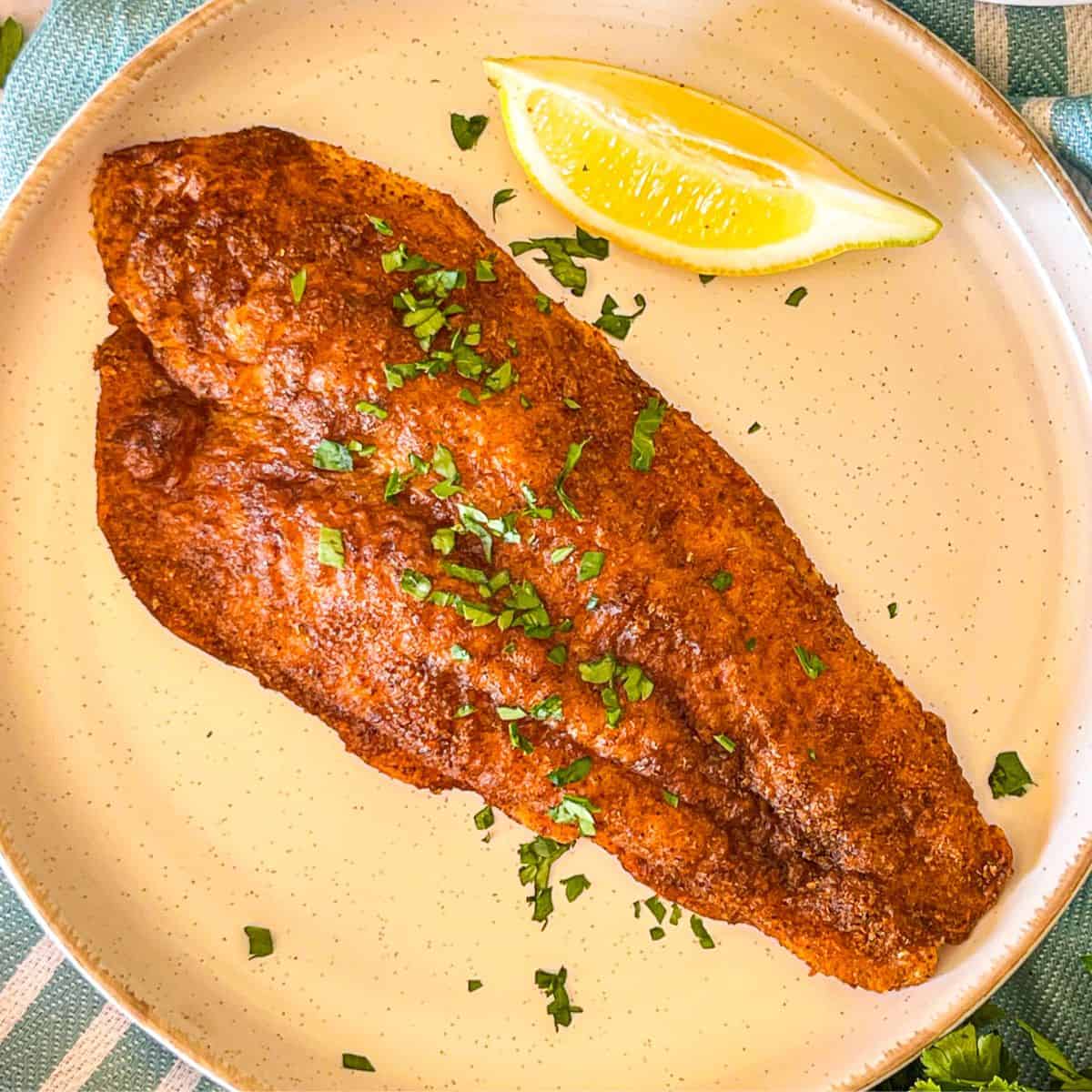 Blackened catfish in a plate and garnished with greens and lemon.