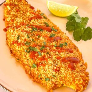 crusted fish on a white platter with dabs of hot sauce.