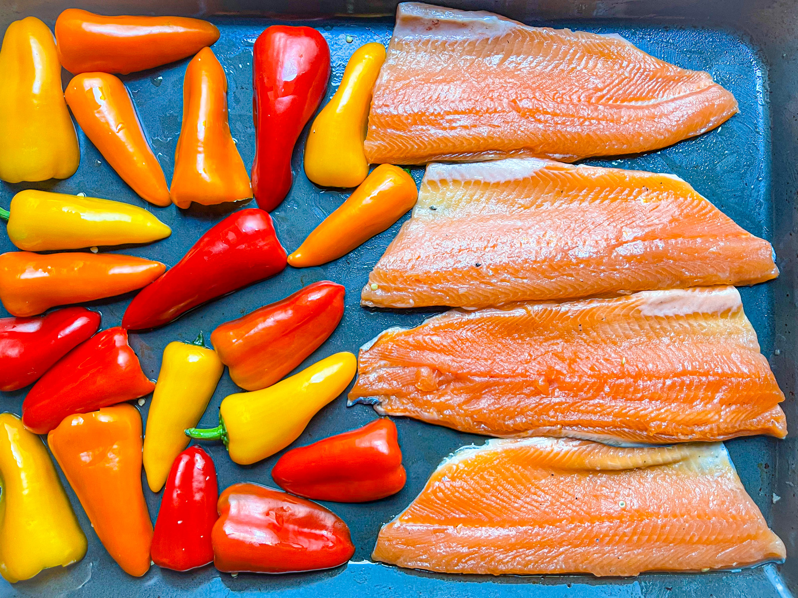 Quatre morceaux de filets de truite posés sur une casserole avec des poivrons multicolores.