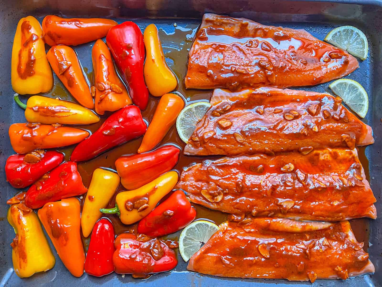 Quatre morceaux de filets de truite posés sur une casserole avec des poivrons multicolores et vitrés avec de la sauce au beurre à l'ail paprika.