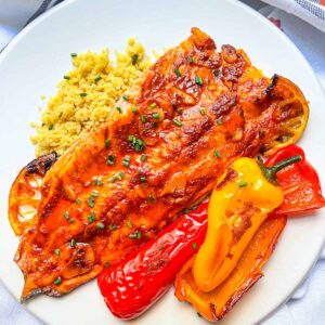 Baked trout glazed with paprika butter sauce on a bed of couscous and roasted multi colored peppers.