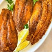 3 morceaux de poisson-chat noircis sur un plateau blanc garni de citron et de persil.
