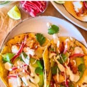 deux tacos au poisson sur une assiette garnie de citrons verts et d'oignons marinés.