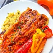 Trout cuit au four vitré avec sauce au beurre paprika sur un lit de couscous et de poivrons multicolores rôtis.