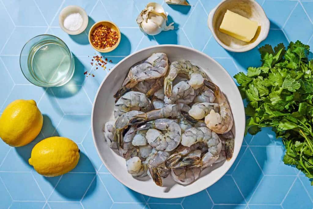 Ingrédients pour la recette de scampi des crevettes, y compris les crevettes, l'ail, le sel, l'huile d'olive, les flocons de poivron rouge, le beurre, le vin blanc, le citron et le persil.