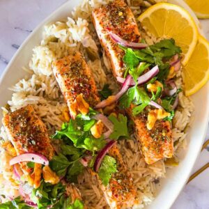4 pieces of salmon on atop of a bed of rice on a white plate.