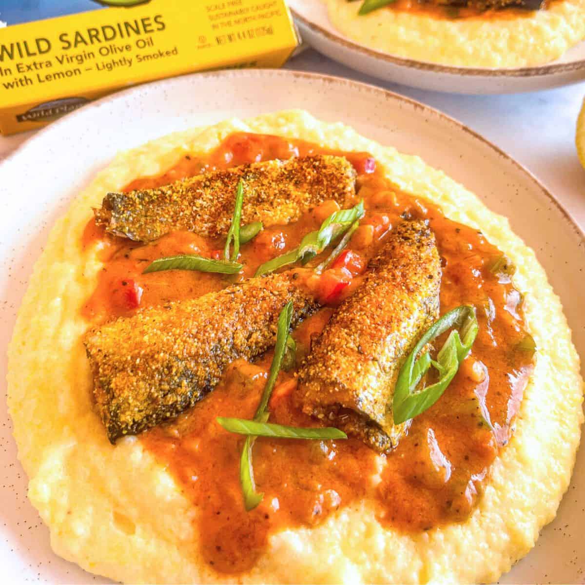 Sardines on top of a plate grits and garnished with green onions.