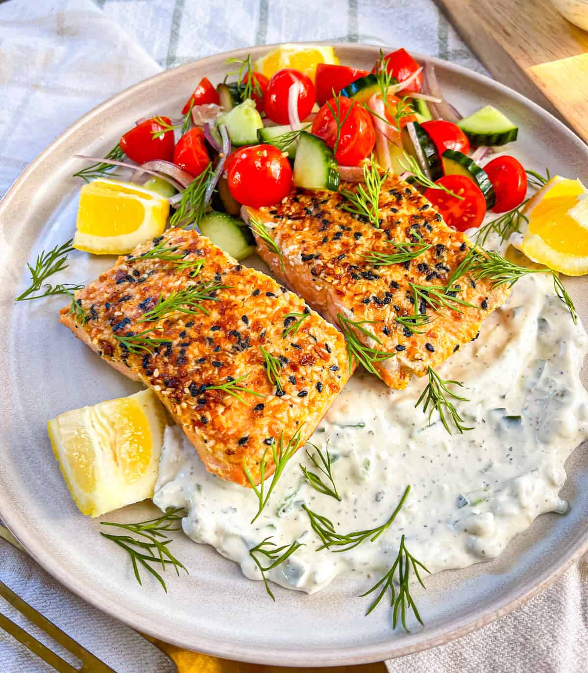 2 morceaux de saumon avec assaisonnement sur un lit de tzatziki et servi avec des légumes et garni de l'aneth.