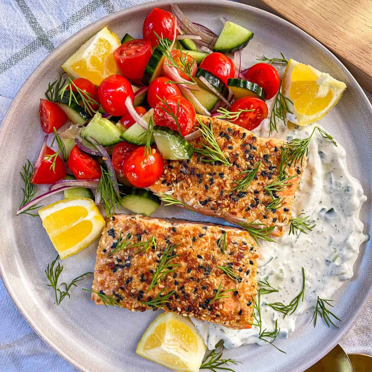 2 pieces of salmon with seasoning on a bed of tzatziki and served with vegetables and garnished with dill.