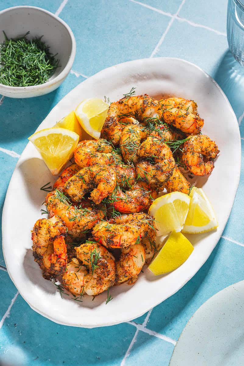 Crevettes de friteuse à air sur un plateau avec des quartiers de citron à côté d'un bol d'herbe à l'aneth.