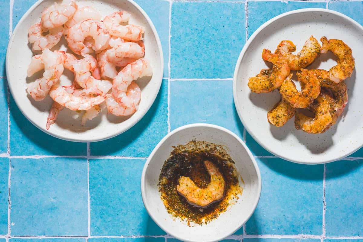 Une assiette de crevettes non munidées à côté d'un bol de marinade contenant une crevette et une assiette de crevettes marinadées.
