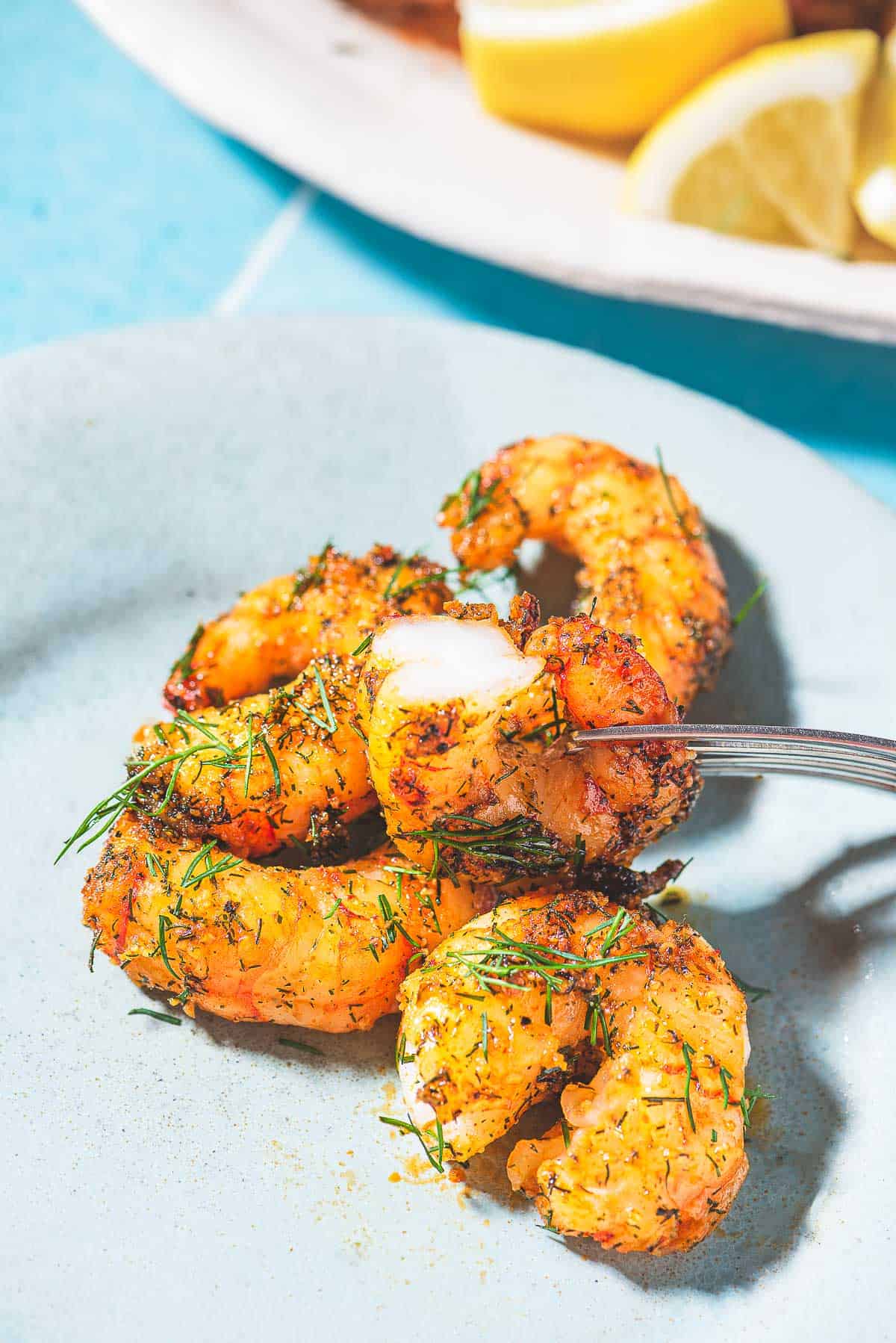 Une fourchette avec des crevettes étant maintenue sur plus de crevettes de friteuse sur une assiette.