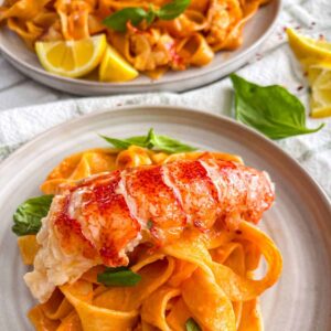 Lobster on a bed of tomato pasta in a white plate.