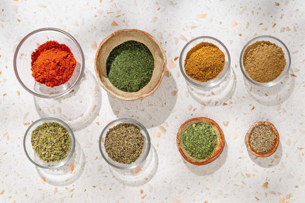 Ingrédients pour l'assaisonnement des poissons, y compris le paprika sucré, l'aneth séché, la coriandre moulue, le cumin moulu, l'origan séché, le thym séché, l'estragon séché et le poivre noir moulu.