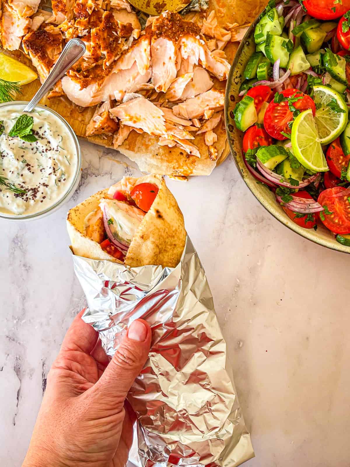 Shawarma Pita enveloppe avec du papier d'aluminium maintenu en main à côté de toute la fixation.