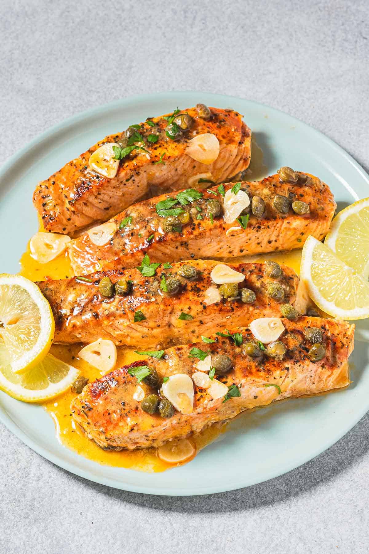 4 filets de piccata de saumon sur une assiette avec des quartiers de citron.