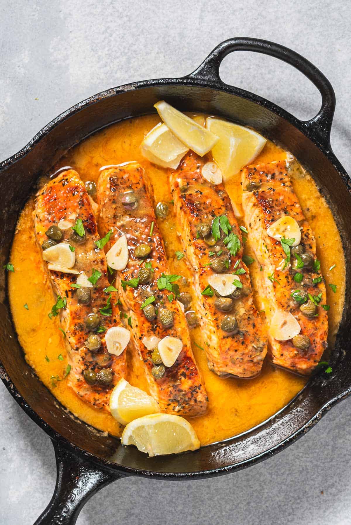 4 filets de piccata de saumon avec la sauce dans une poêle en fonte avec des quartiers de citron.